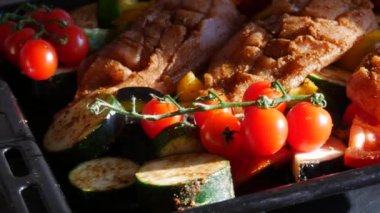A raw large piece of chicken breast just ready to oven baked with vegetables, cherry tomatoes, zucchini, eggplant, paprika on a baking sheet close up view.
