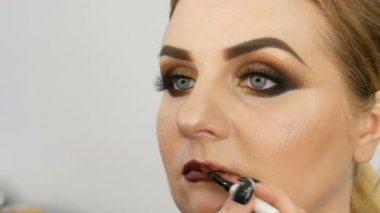 Profesyonel usta makyaj sanatçısı güzellik salonunda özel fırça ve makyaj dumanlı gözleri ile model ince dudaklar koyu kırmızı ruj uygular