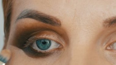 Profesyonel makyöz, mavi gözlü genç bir kadın manken için özel fırçayla bej makyaj yapıyor.