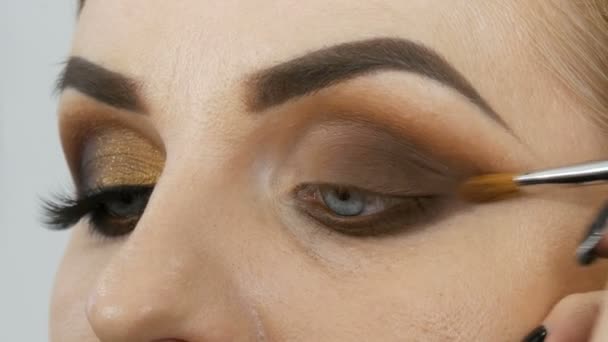 大师化妆师在美容院里用专业的化妆黄金烟熏眼睛给蓝眼睛模特配上蓝眼睛 — 图库视频影像