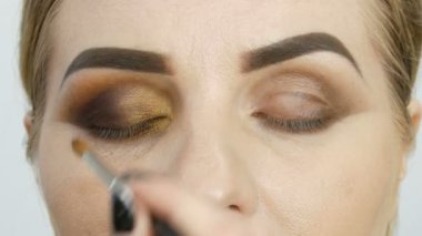 Makyaj ustası bir güzellik salonunda mavi gözlü model bir kadına profesyonel makyajlı altın dumanlı gözler uygular..
