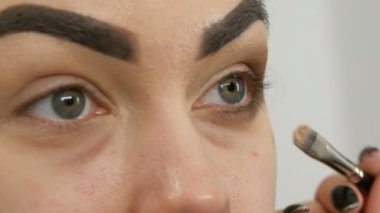 Profesyonel makyöz, kahverengi bir gölgenin dumanlı gözlerini yeşil gözlü güzel bir modelin özel fırçasıyla yapar.