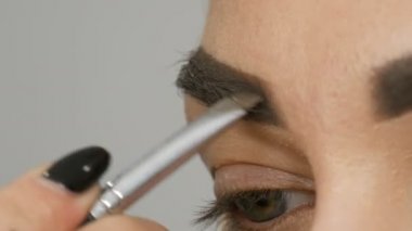 Makyaj sanatçısı, model kızları güzellik salonunda profesyonel makyaj malzemesi yapar. Özel bir fırçayla kaş çizimi