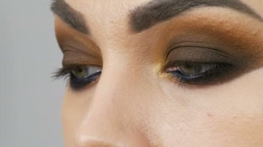 Profesyonel makyöz, kahverengi bir gölgenin dumanlı gözlerini yeşil gözlü güzel bir modelin özel fırçasıyla yapar.