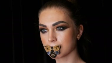 Güzel, profesyonel bir kız modelin portresi şık dumanlı göz makyajı ve stüdyoda kameranın önünde poz veren dudaklarında kelebek. Yüksek moda.