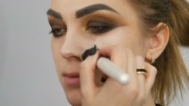 Makyaj sanatçısı, bir güzellik stüdyosunda modellik yapıyor. Cildine fırçayla kapatıcı sürüyor.