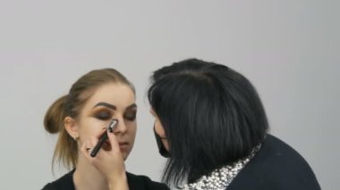 Profesyonel makyöz, kahverengi bir gölgenin dumanlı gözlerini yeşil gözlü güzel bir modelin özel fırçasıyla yapar.