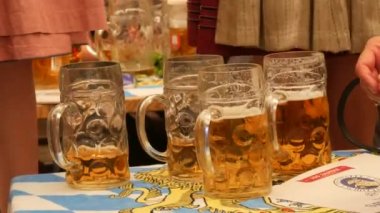 Münih, Almanya - 17 Eylül 2022: Ekim Festivali çadırlarından biri. İnsanlar geleneksel Oktoberfest kostümleri içinde bira ve yemek bardaklarıyla çevrili bir masada durup dans ediyorlar..