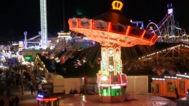 Münih, Almanya - 17 Eylül 2022: Renkli parlayan binişler, atlıkarıncaların ve salıncakların gece görüşü. Dünyaca ünlü bira festivali Oktoberfest 'in ziyaretçileri. Theresienwiese 'deki kalabalık.