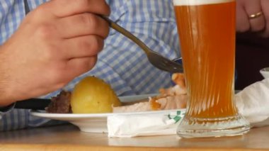 Oktoberfest çadırları. Bir adam bir bardak bira içer ve bıçak ve çatalla geleneksel domuz budu ile lahana turşusu ve kızarmış patates yer. Münih, Almanya.