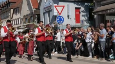 Buhl, Almanya - 11 Eylül 2022: Şehir sokaklarındaki erik hasadının onuruna düzenlenen şenlik geçidi. Kırmızı yelekli güzel giyimli bir orkestra rüzgâr enstrümanları çalıyor ve bir sütun halinde yürüyor..