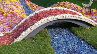 Kasımpatı köprüsünün ve cam parçalarından yapılmış bir ağacın güzel kurulumu. Parkta sonbahar kasımpatı festivali. Turuncu, beyaz, pembe, çeşitli çiçekler.