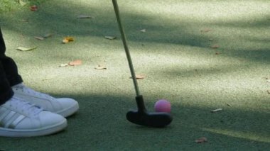 Mini golf. Üzerinde golf sopasıyla vurulan pembe bir topun bulunduğu yapay çim ile kaplı yeşil bir alan. Suni yeşil çim kortunda golf topu