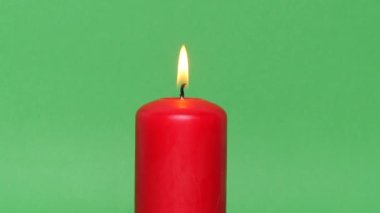 Yeşil krom anahtar arka planında koyu kırmızı bir Noel mumu. Mum alevi yanıyor ve dans ediyor..