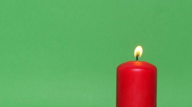 Yeşil krom anahtar arka planında koyu kırmızı bir Noel mumu. Mum alevi yanıyor ve dans ediyor..