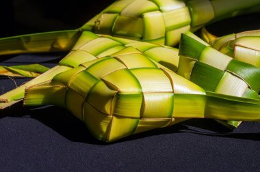 Ketupat, koyu arkaplanda hindistan cevizi yapraklı elmas kabın içinde pirinç keki var.