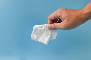 El ele tutuşan buruşmuş kağıt parçası mavi arka planda izole edilmiş.