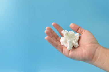 El ele tutuşan buruşuk doku, mavi bir arka planda izole edilmiş. Hijyen, sağlık ve güvenlik kavramı.