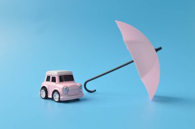 Pembe oyuncak şemsiye ve oyuncak araba mavi arka planda izole edilmiş.