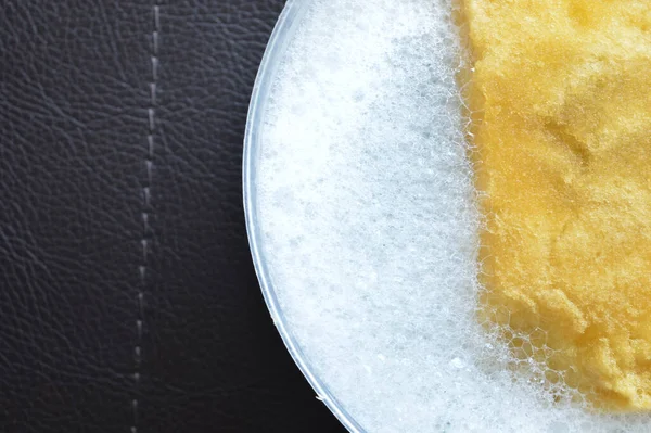 Sarı sünger ve sıvı sabun köpüğü siyah arkaplanda izole edilmiş.