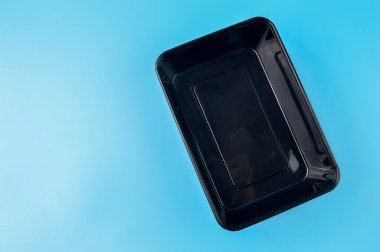 Mavi arka planda izole edilmiş siyah plastik yiyecek kabı.