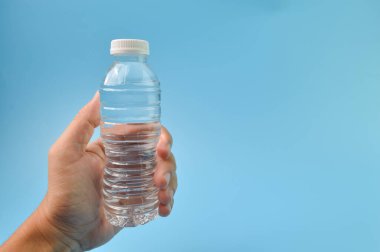 Hand holding mineral water isolated on a blue background. Copy space for the text