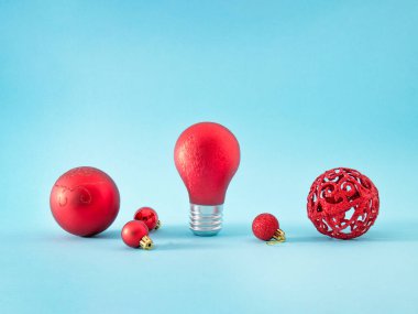 Pastel mavi arka planda yeni yıl ağacı için kırmızı süsleme topları. Bir top parlayan bir ampuldür. Yaratıcı Kış Konsepti.