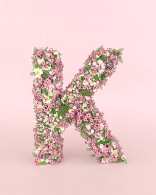 Creative letter K concept made of fresh Spring wedding flowers. Flower font concept on pastel pink background.
