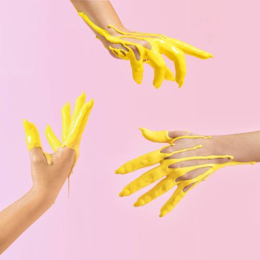 Havadaki sarı boyaya batırılmış el kaldırma fikri yaratıcıydı. Pastel pembe arkaplan.