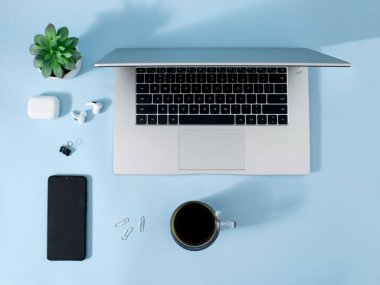 Yaratıcı ofis ortamı ve evde çalışmak için çalışma ortamı. Kahve, laptop, telefon ve kulaklıklar pastel mavi masa arkasında..