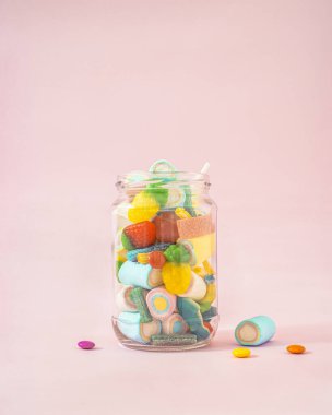Creative concept of a glass jar full of delicious sweets from the candy store. Pastel pink background.