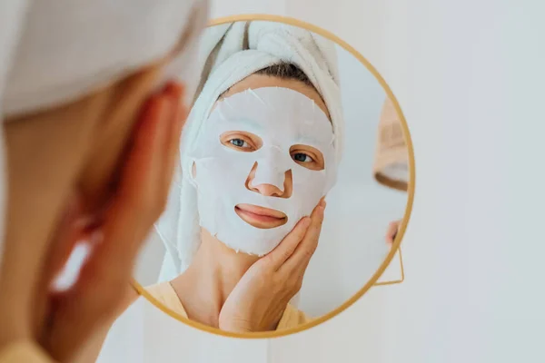 Mulher Com Lençol Hidratante Máscara Facial Olhando Espelho Tratamentos Faciais — Fotografia de Stock