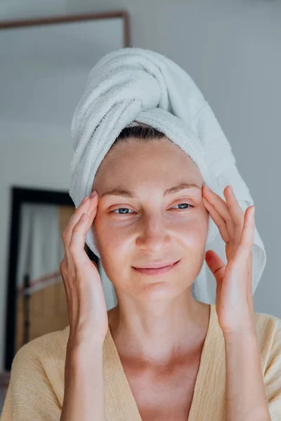穿着浴衣 头戴毛巾的年轻女人在按摩她的脸和头 自我照顾的概念 — 图库照片