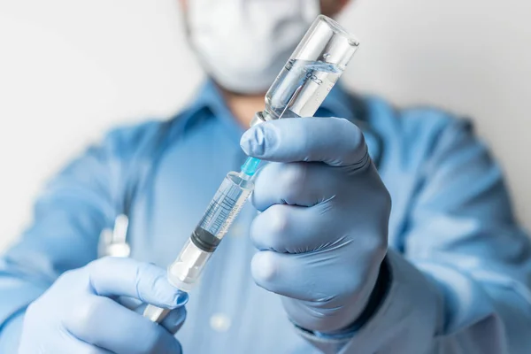 Male, doctor in blue shirt and gloves, holding in the hand a syringe and vaccine bottle against disease coronavirus or flu, vaccination concept.