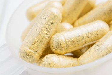 Plastik kaşıkta sarı bitkisel kapsüller, ilaç tedavisi, alternatif tıp, yakın çekim.
