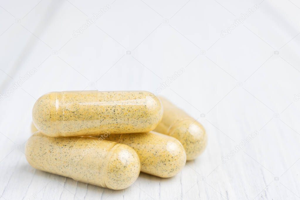 Yellow herbal capsules on white table, medication treatment, alternative medicine, close-up view.