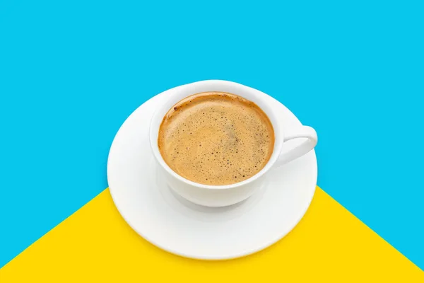 底色为蓝色和黄色 盘中白杯中泡沫的黑咖啡 — 图库照片