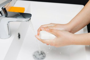 Banyoda sabunla musluğun altında ellerini yıkayan genç bir kadın, hijyen kavramı..