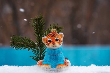 Dışarıda Noel ağacı oyuncağıyla kaplan yavrusu. Kar taneleri düşüyor. Arka plan bulanık. 2022 yılının sembolü..