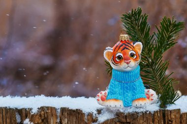 Dışarıda Noel ağacı oyuncağıyla kaplan yavrusu. Kar taneleri düşüyor. Arka plan bulanık. Mutlu noeller. 2022 yılının sembolü..