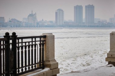 Amur nehri üzerindeki Blagoveshchensk şehrinin kışın manzarası buzla kaplıdır. Kar yağıyor. Heihe City, Çin binaları. Seçici odak.