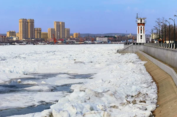 Rusya 'nın Blagoveshchensk kentinde deniz feneri. Heihe şehri manzarası, Çin. Amur Nehri buz kütleleriyle kaplıdır. Buz kayması dönemi. Siyah su. Kış sonu. Güneşli.