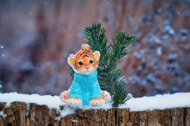 Parlak turuncu kaplan yavrusu bir orman kütüğünün üzerinde doğal bir ladin dalıyla. Kar taneleri düşüyor. Mavi örülmüş süveter. Mutlu noeller. Mutlu yıllar 2022.