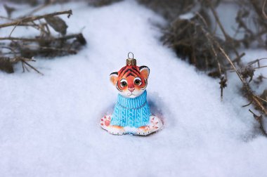 Yeni 2022 'nin sembolü olan oyuncak bir kaplan, beyaz kar üzerinde mavi bir kazakla ormanda oturuyor. Noel ağacı süslemesi. Arka planda kuru bitkiler var. Mutlu noeller. Seçici odak.