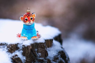 Ormanda, karla kaplı bir kütüğün üzerinde mavi süveter giymiş Noel ağacı oyuncağı kaplan. Mutlu noeller. Mutlu yıllar 2022.