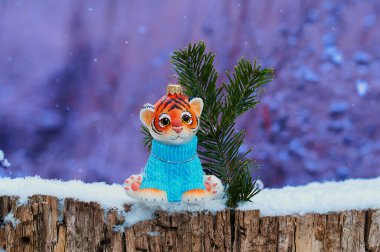 Mavi kazaklı güzel bir kaplan yavrusu karlı bir ormanda bir ladin dalının yanında bir kütüğün üzerinde oturuyor. Geçmişi 2022 Çok Peri renginde. Mutlu Çin Yeni Yılı 2022. Metin için yeri olan tebrik kartı.