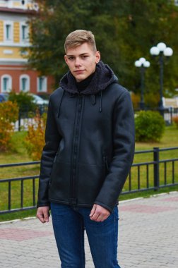 A young guy walks down the street in a warm jacket with a hood and jeans. Early autumn. Selective focus. Blagoveshchensk, Russia.