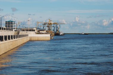 Amur river embankment. Increased water level in the Amur River. Port cranes and passenger customs in the background. Summer sunny day. Blagoveshchensk, Russia.