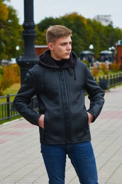 A serious blond man in a leather jacket stands on the city embankment against the backdrop of a rotunda. Blur the background. Blagoveshchensk, Russia.