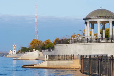 Rotunda and lighthouse on the embankment of the city of Blagoveshchensk, Russia in autumn 2021. Increased water level in the Amur River after the summer flood. Yellow foliage of trees in a city park.